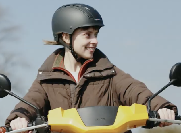 Das Foto zeigt eine Frau auf einem gelben Roller.