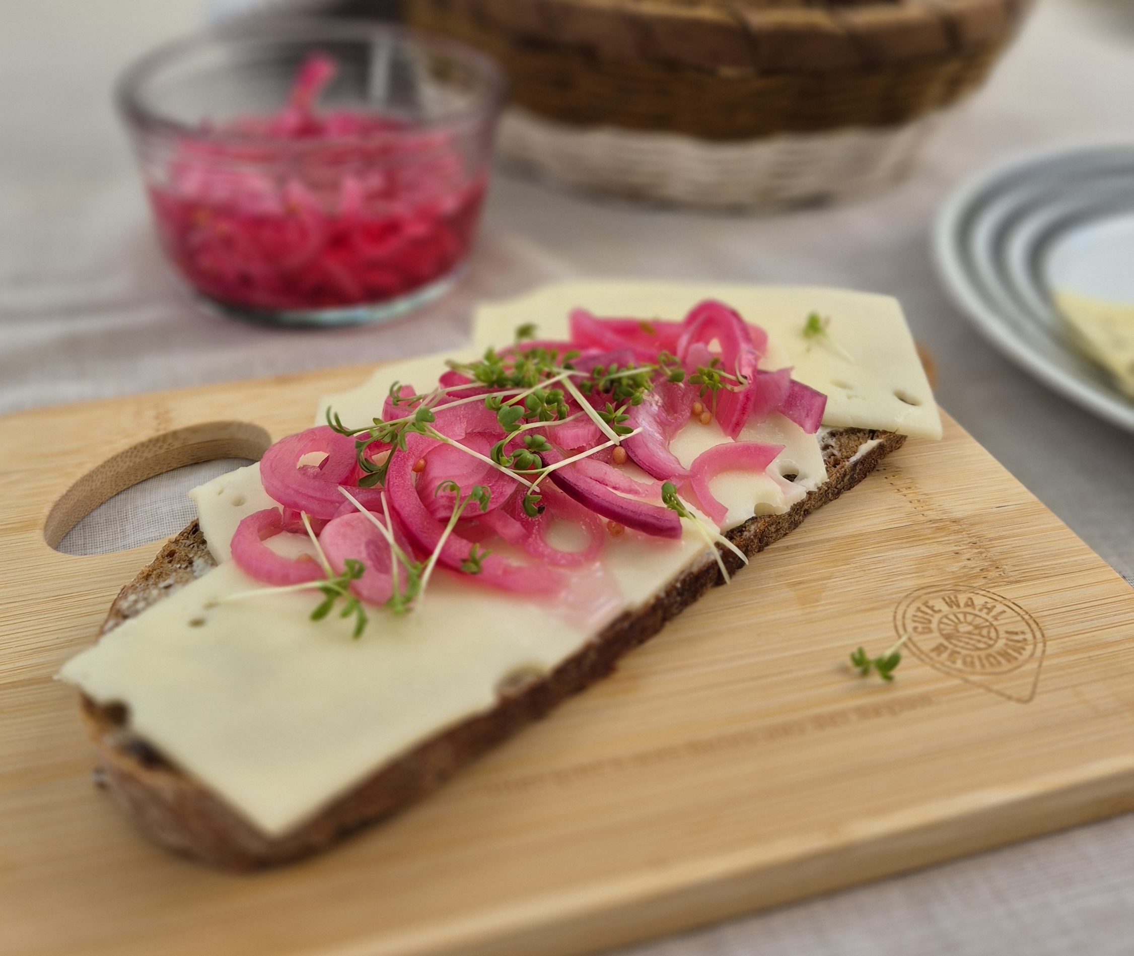 Das Foto zeigt eine Scheibe Brot mit Käse und eingelegten Zwiebeln.