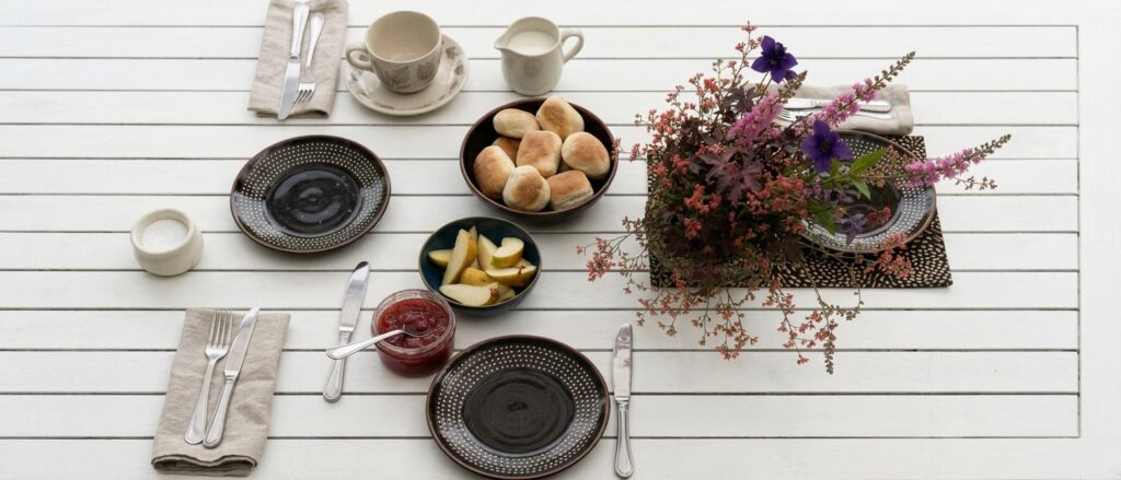 Das Foto zeigt einen Frühstückstisch mit frischen Brötchen, geschnittenen Äpfeln und Marmelade