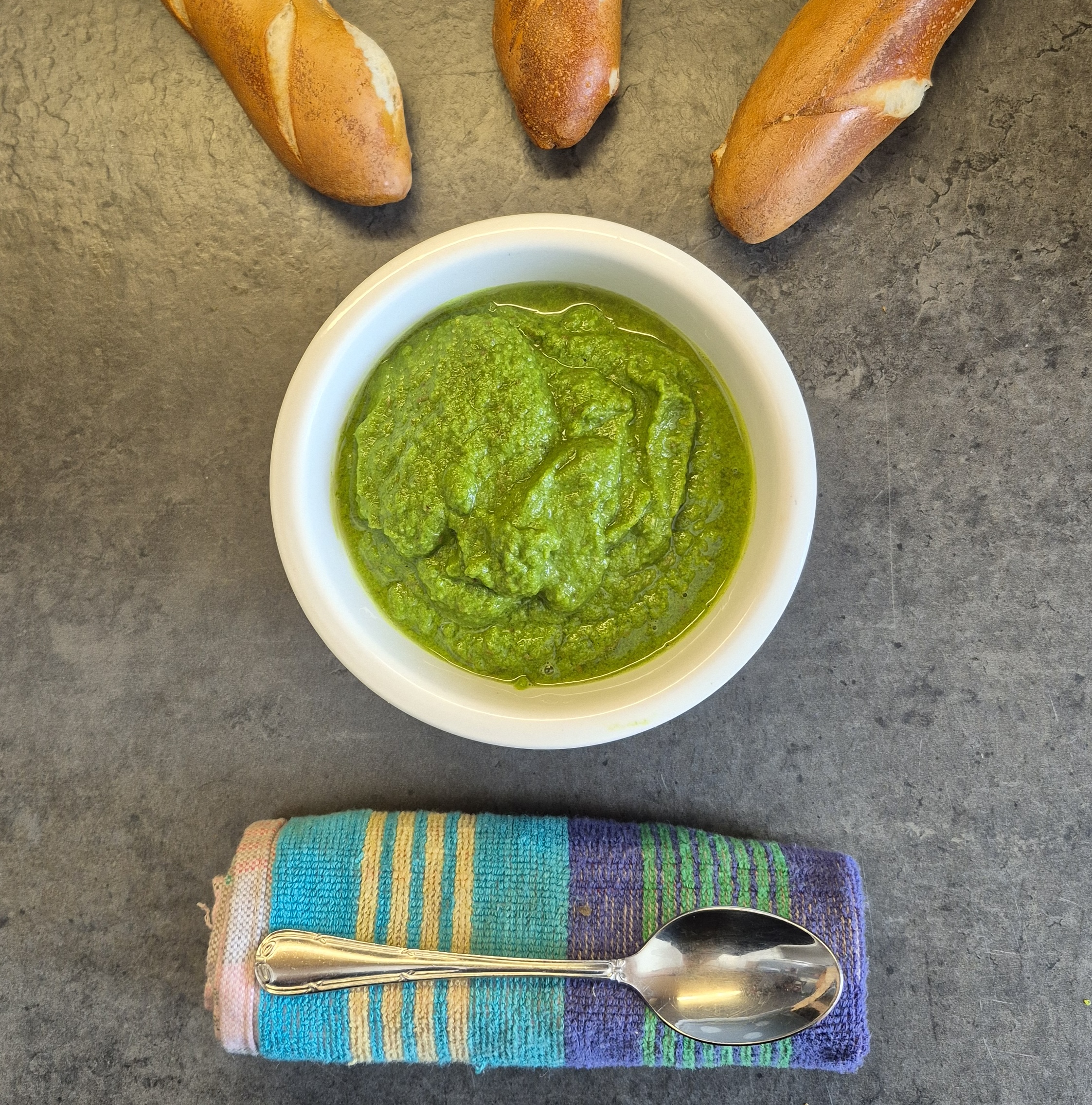 Das Foto zeigt eine Schale mit grünem Pesto und drei Baguettes.