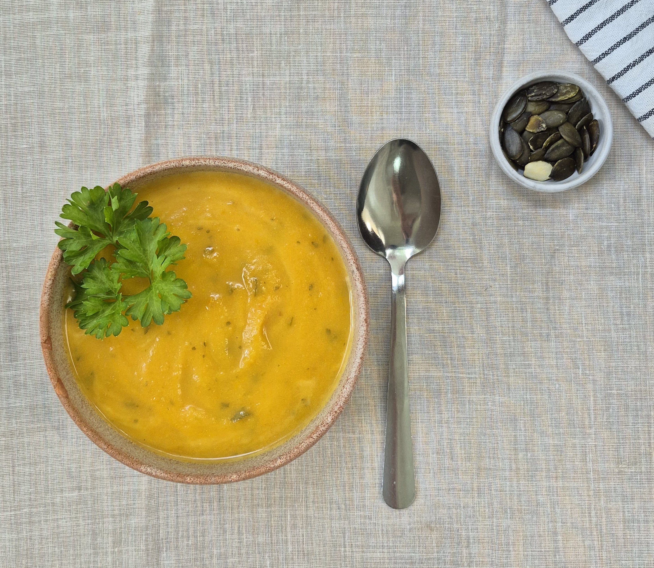 Das Foto zeigt eine Schale mit Kürbissuppe und eine kleine Schale mit Kürbiskernen.